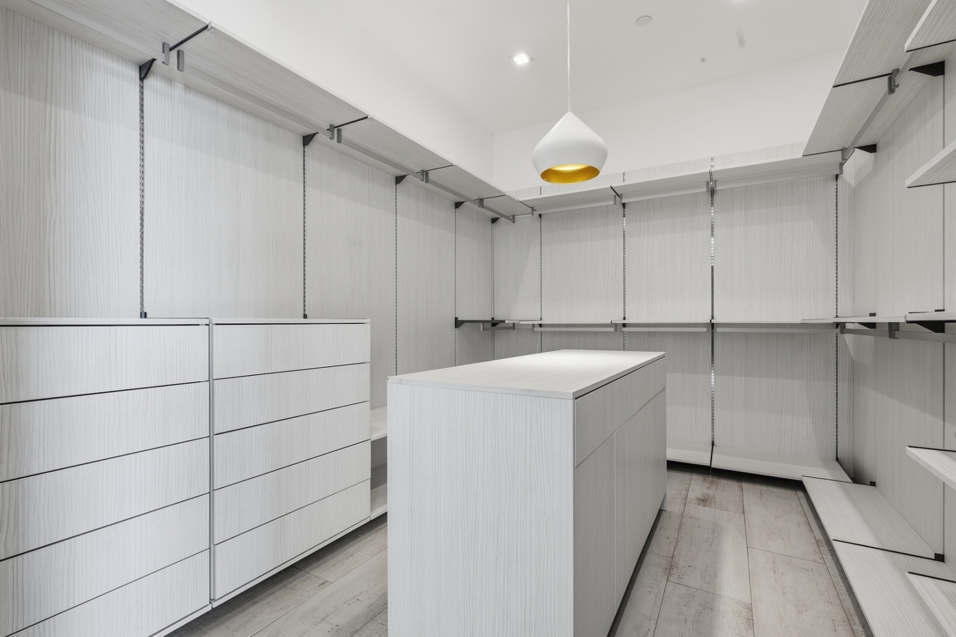 Closet with white wood shelving, hanging storage, and drawers around a central island.