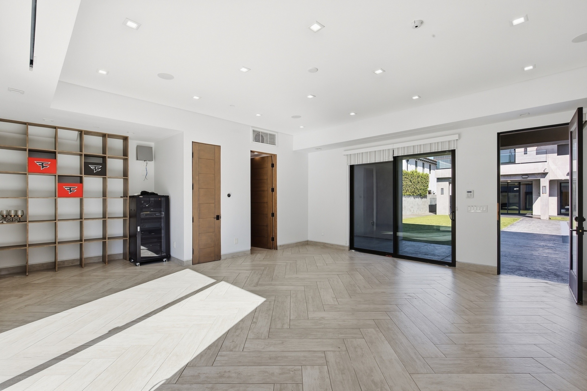 The lower level opens into a living area with herringbone-patterned flooring, built-in shelving, and large glass doors that connect directly to the courtyard.
