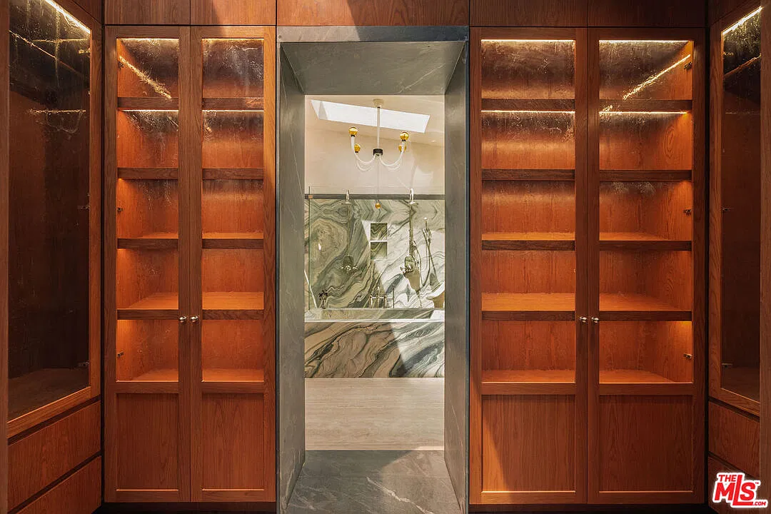 A dressing room with illuminated display shelving right before the marble bathroom.