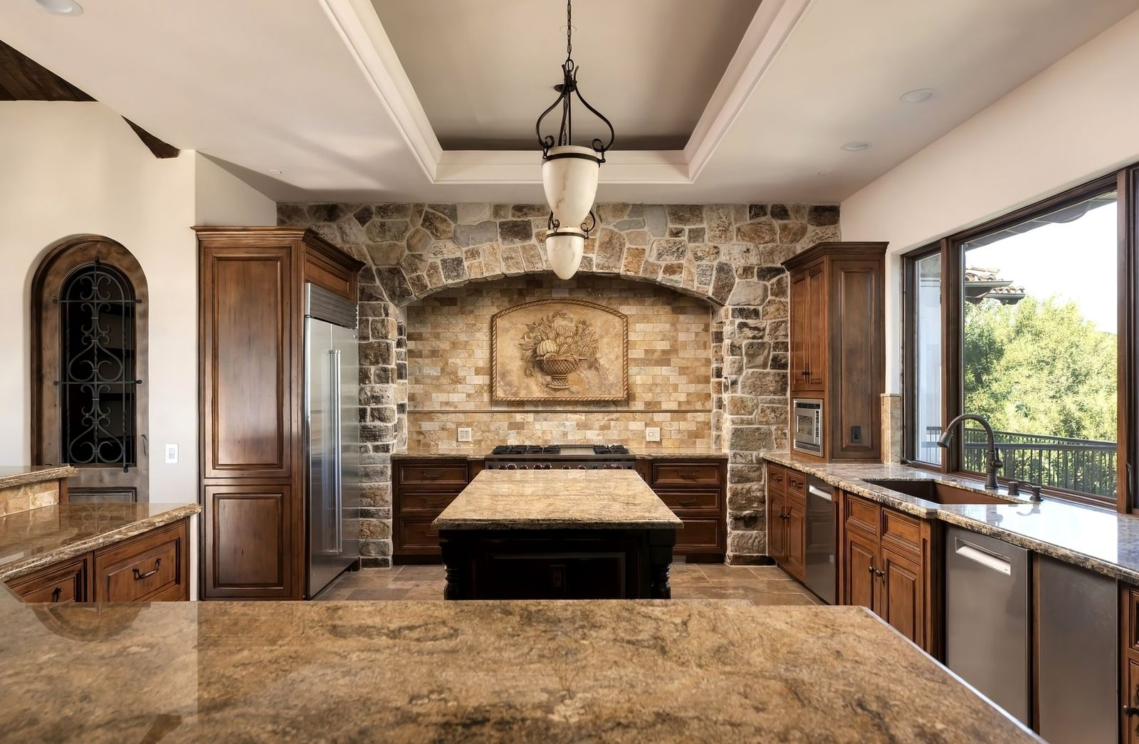 Across from the island, one entire wall is made up of stone with an arch cutout that holds the oven and stovetop.