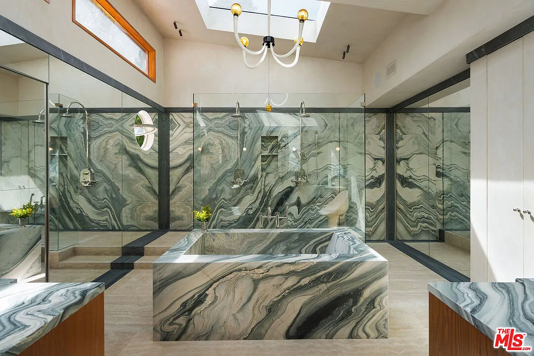 A freestanding tub wrapped in the same marble sits in the center beneath skylights before stepping up to the glass-enclosed shower at the back of the room.