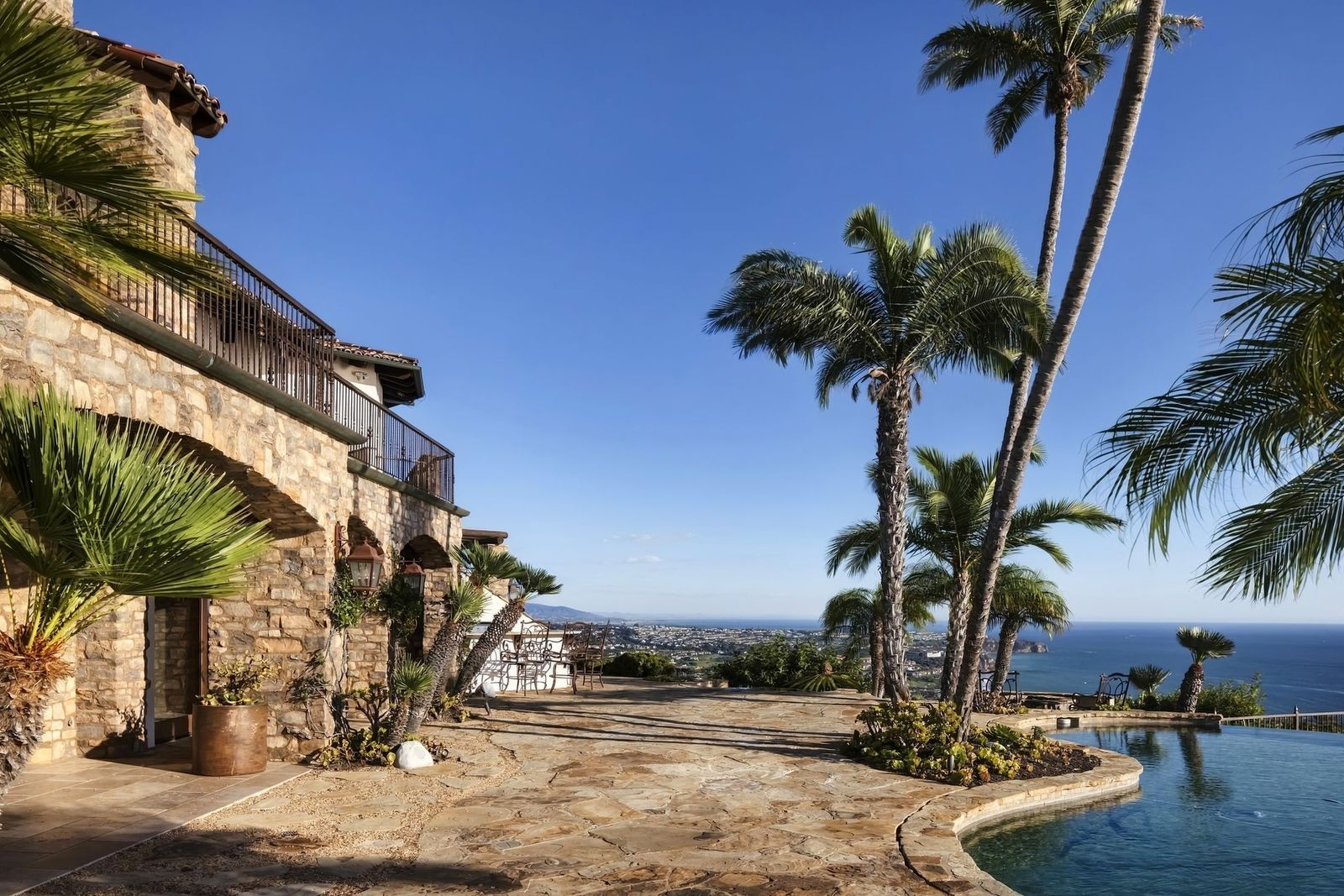 An outdoor bar and built-in barbecue sit close to the covered terrace, while a separate firepit area is placed right along the edge of the pool.