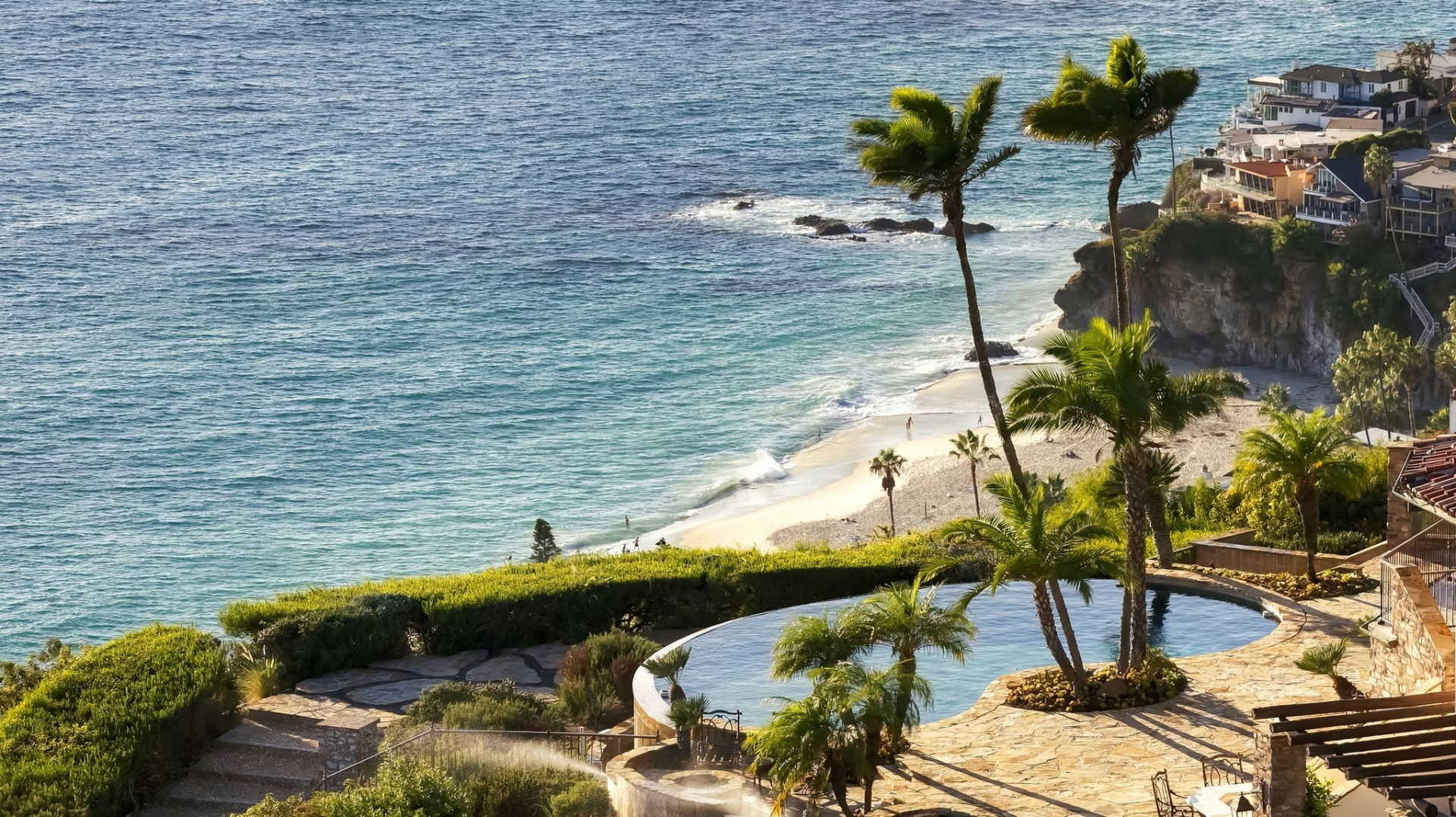 The terrace opens around an infinity-edge swimming pool at the edge of the property framed by palm trees and low landscaping.