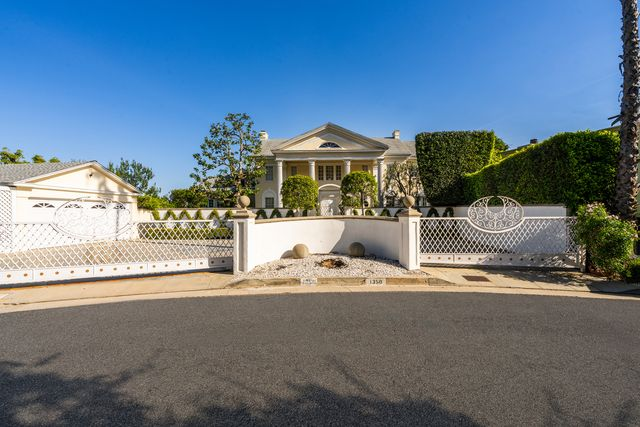 A long white privacy wall, with trimmed trees rising above it and just a hint of the estate visible.