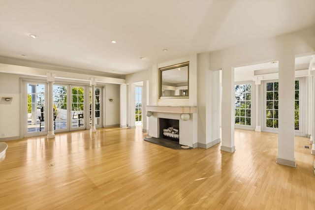 A double-sided fireplace sits in the center of the room, separating the living room from the music room, which is enclosed almost entirely by floor-to-ceiling windows.
