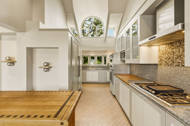 Thermador appliances are built into the sleek cabinetry with frosted-glass upper cabinets, while a mosaic tile backsplash adds texture behind the cooktop.