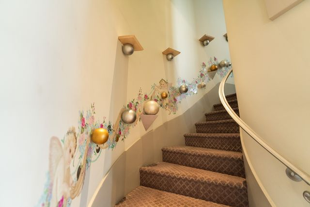 The curved staircase guides you up steps carpeted in a diamond pattern and walls lined with whimsical spheres and a mural of angels and flowers.
