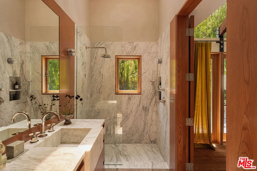 Bathroom is lined in white marble, with a long vanity running along one side and a large walk-in shower extending across the back.