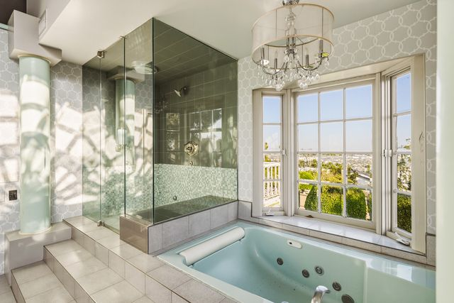 A step-up jetted tub sits beneath a crystal chandelier next to a large glass-enclosed shower.