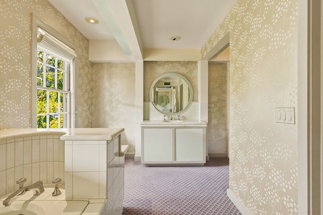 This suite's bathroom includes a tiled soaking tub, a marble vanity beneath a rounded mirror, and a separate walk-in shower.
