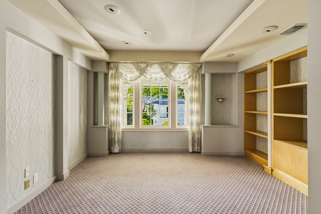 A wall of built-in shelving lines one side of the room, while a large window alcove at the far end brings in soft light.
