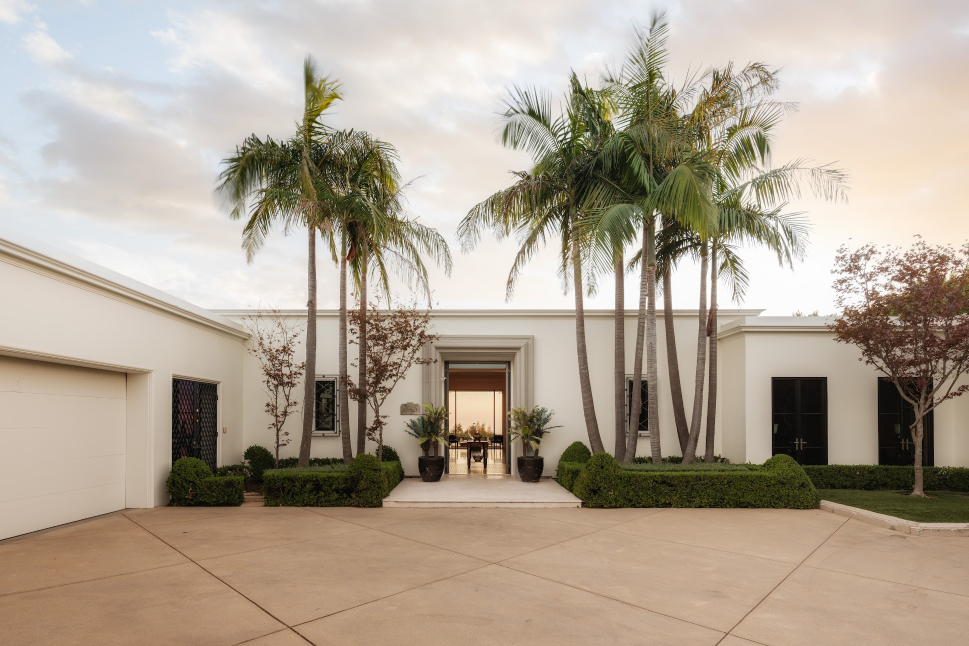 An unusually wide motor court, where olive trees, palm trees, and landscaped greenery welcome you up to the front door.