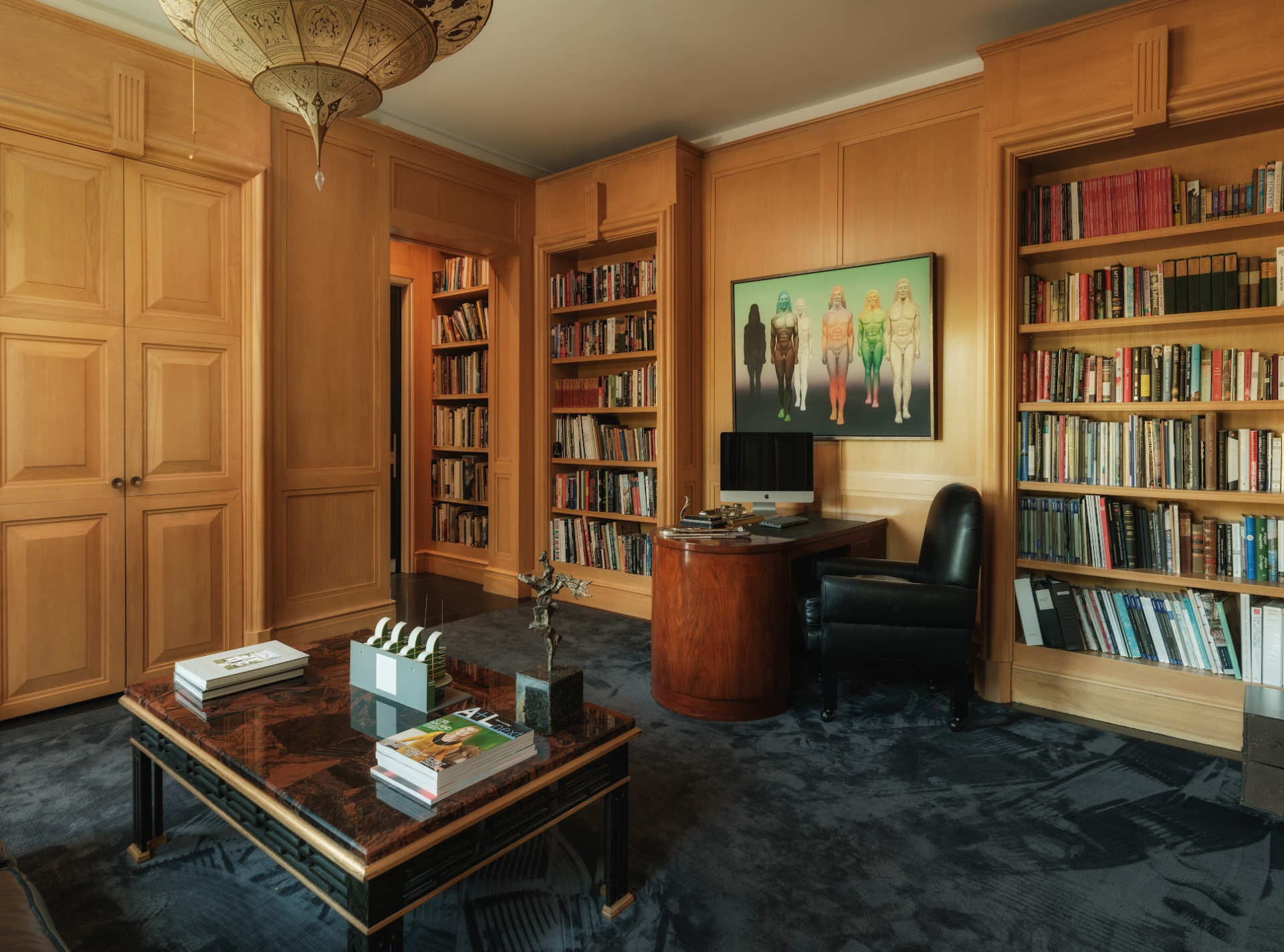 The office is wrapped in warm wood paneling and floor-to-ceiling built-in bookcases framing a curved desk in the center of the room.