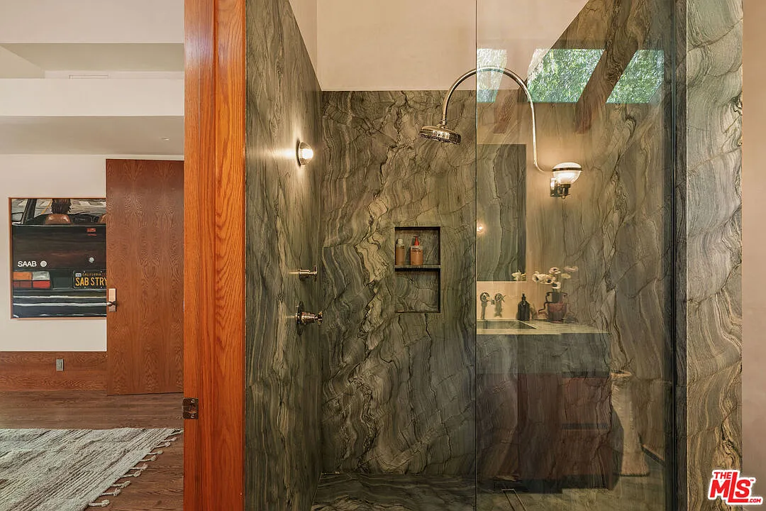 The en-suite bathroom is lined in a dark green marble surrounding a glass-enclosed shower and continuing across the vanity.