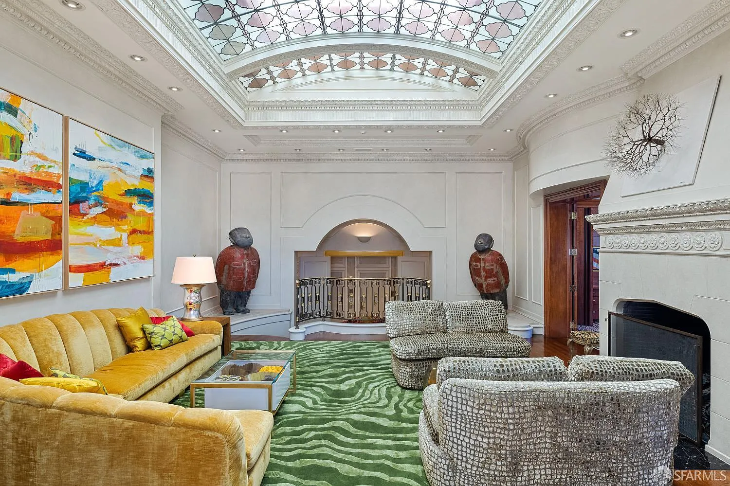 A long yellow couch and snake-skin patterned chairs sit atop a green rug, all gathered around the fireplace.