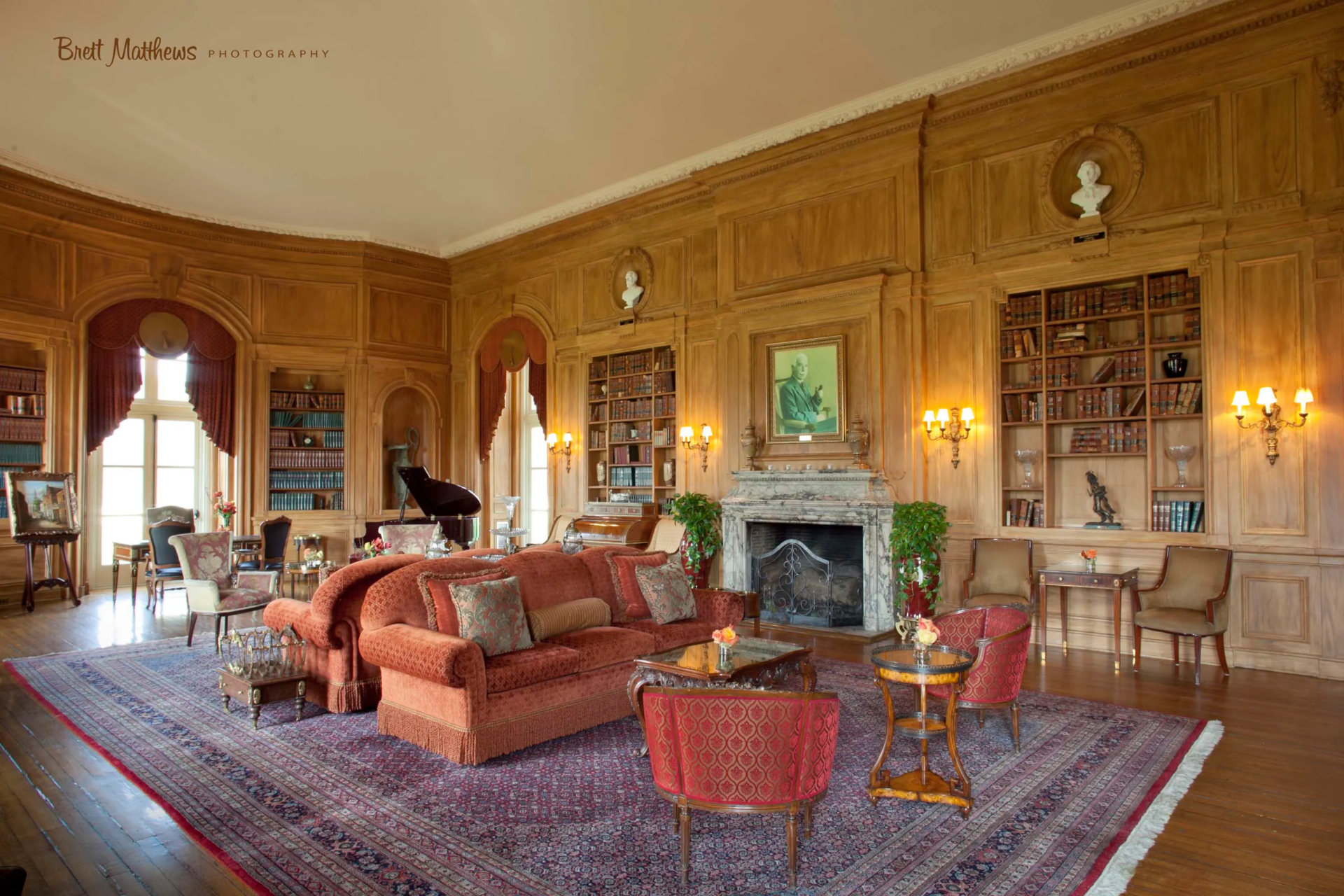 The restored library where hand-finished faux-bois walls wrap the room from floor to ceiling and are broken up by built-in bookcases and arched window bays.