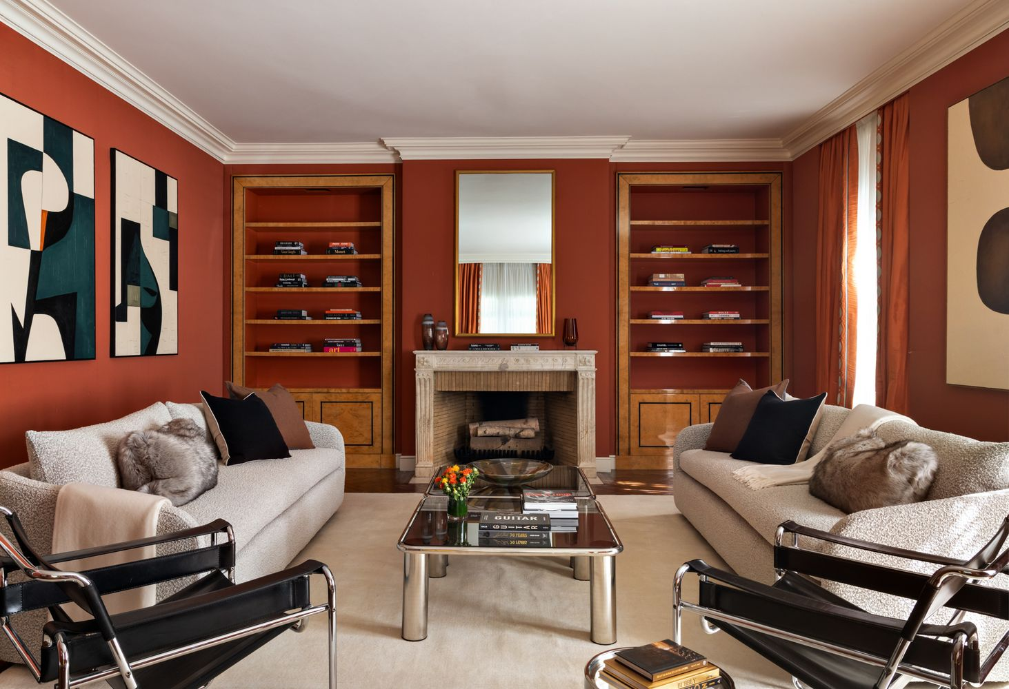 A deep red-painted library with a fireplace centered between a pair of built-in bookcases. 