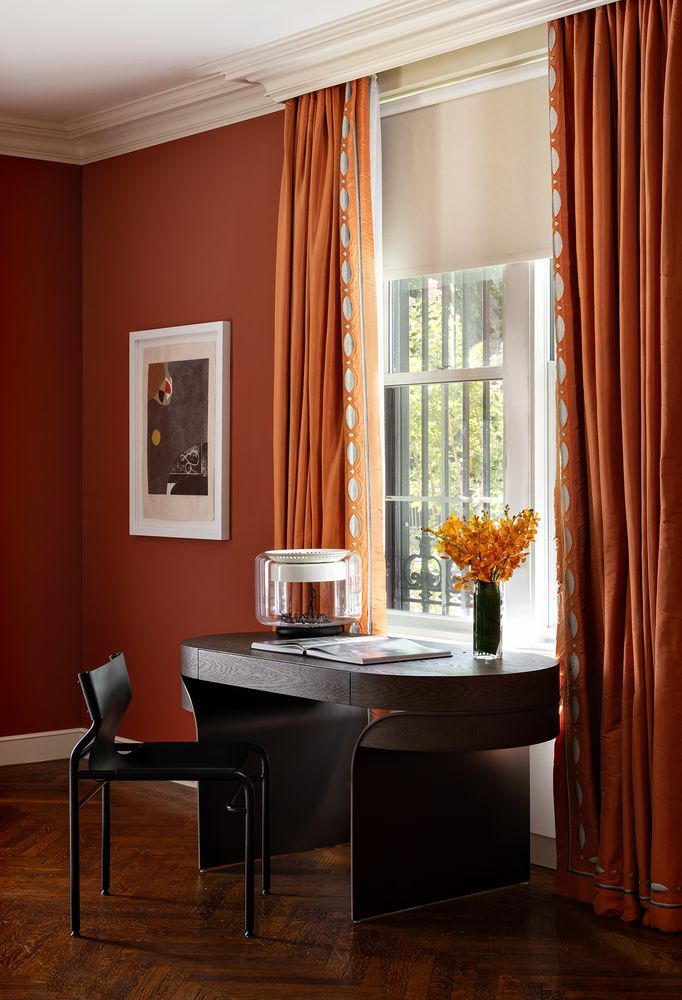 Along one of the windows, the library extends into a small writing desk between floor-length orange curtains that look out to the street.