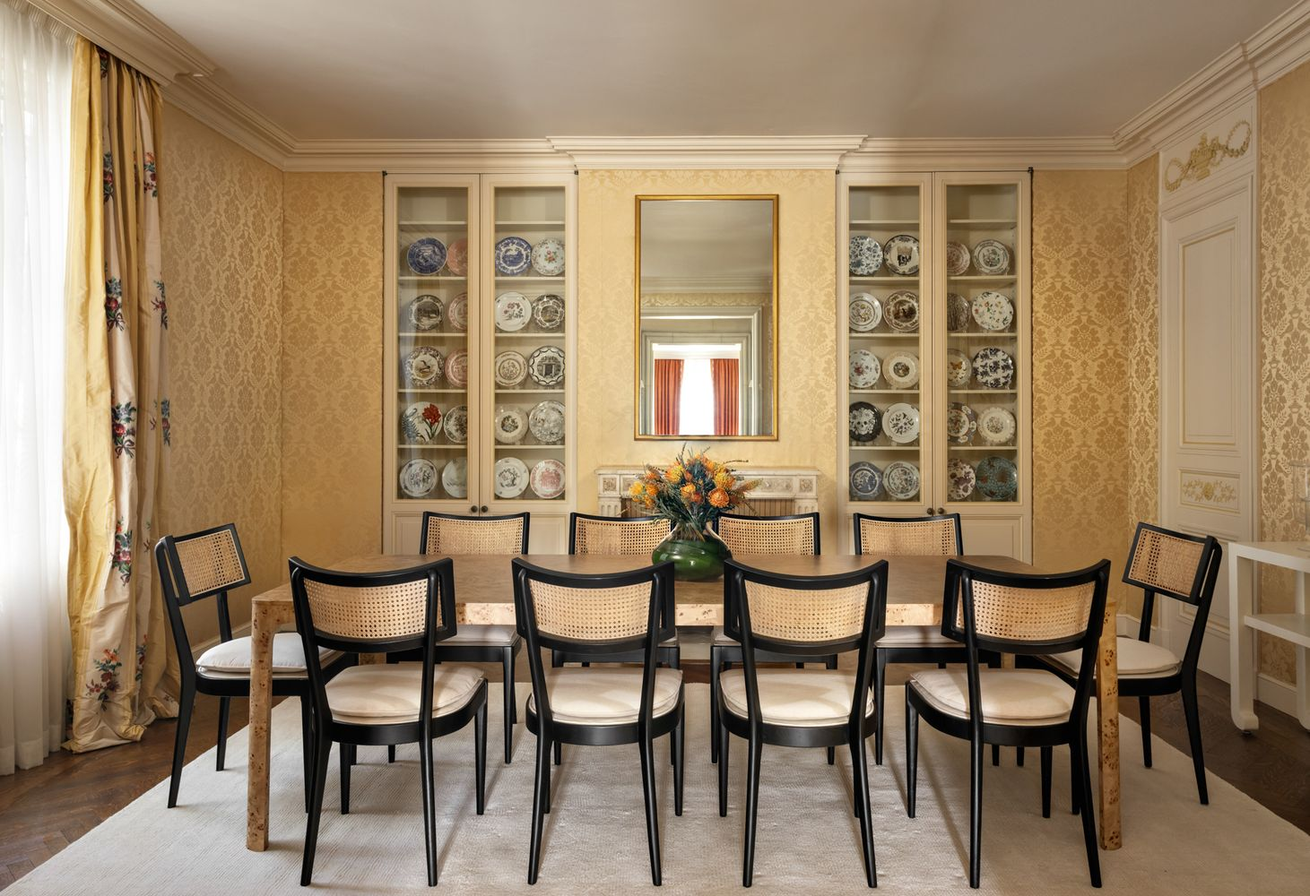 The formal dining room's long rectangular table is surrounded by black-framed cane chairs with a China cabinet behind it.