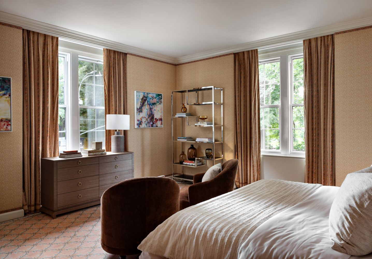 The bedroom arranged between tall windows and a small seating area near the foot of the bed. 