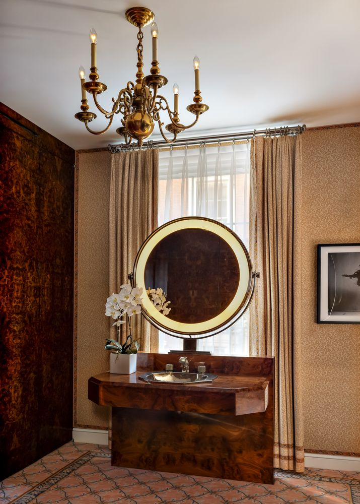 tthe vanity is set in front of one of the windows with a large circular mirror sitting atop a marble wood-like sink.