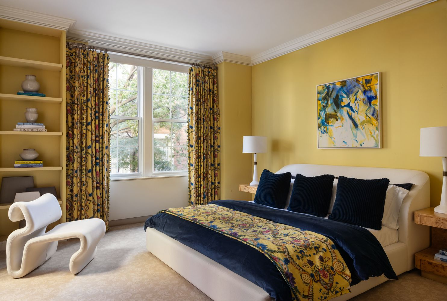 The second suite has a brighter yellow palette, with built-in shelving along one wall and patterned drapery framing the window beside the bed.