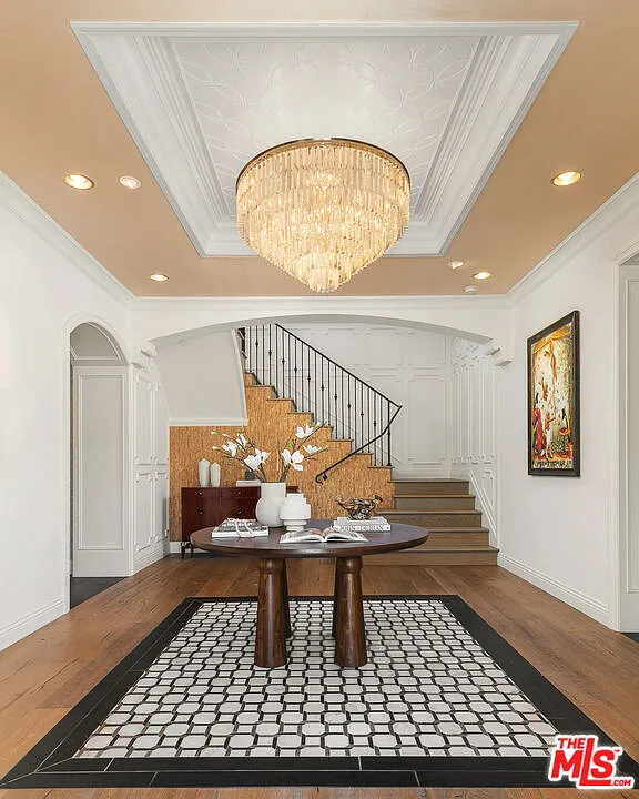 A cascading glass chandelier casting light across wide-plank wood floors and a section of geometric marble at the center of the entry.