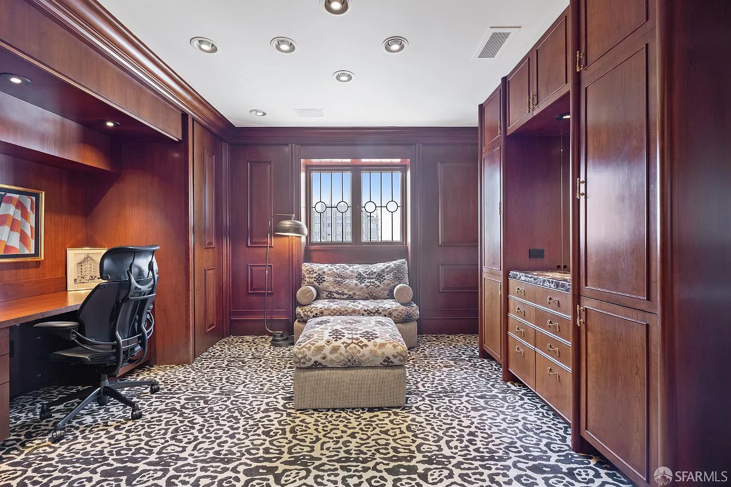 Across the office, the space opens around a recessed desk area, while a lounge chair and ottoman sit beneath the center window to create a separate reading spot.