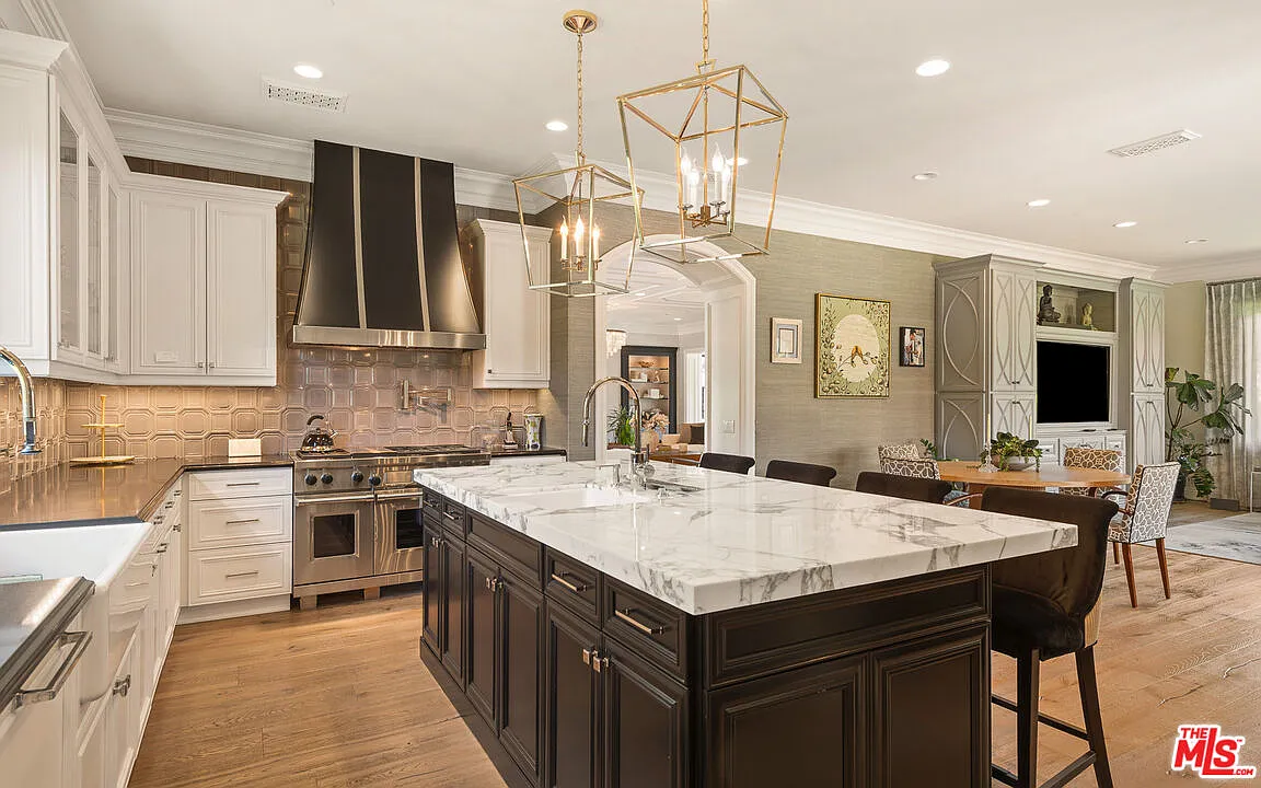 Through an arched doorway, the chef’s kitchen opens to a large marble-topped island, with premier Wolf, Sub-Zero, and ASKO appliances placed around the white cabinetry.