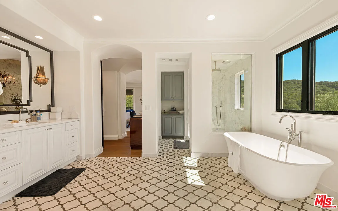 Bathroom stretches across patterned tile flooring, with a freestanding soaking tub sitting next to the walk-in steam shower wrapped in marble.