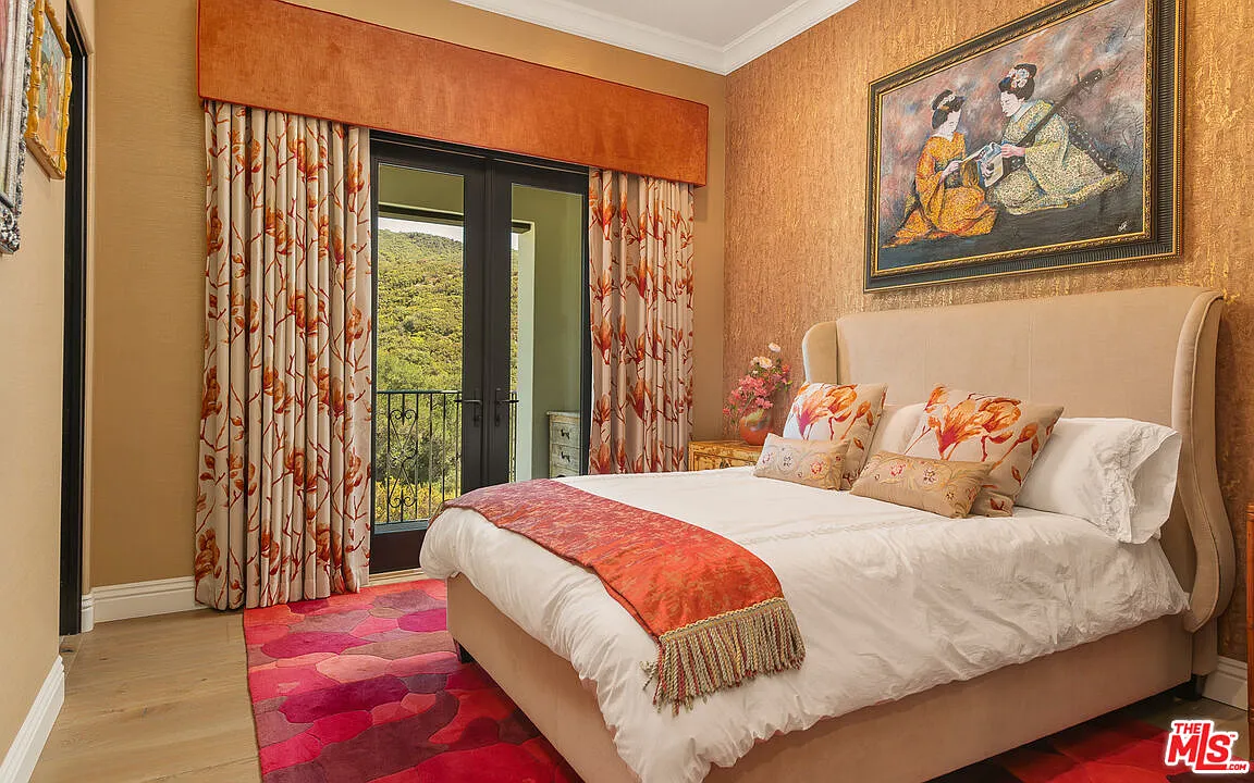 The bed sits in the center of the room beneath a large framed painting, with a bright pink patterned rug underneath it.